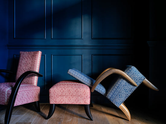 Two red chairs and one blue on tilting backwards in front of an indigo wall 