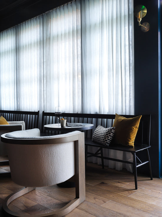 Modern interior with round white table and chairs against a dark wall with light filtering through sheer curtains.