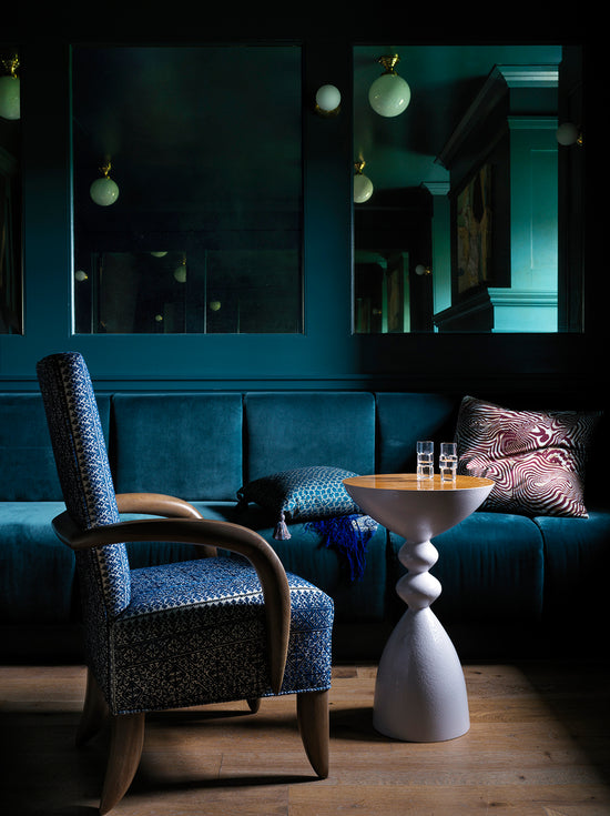 Dark-themed room with a blue armchair, white snap side table with a white oak finish, and decorative pillows.
